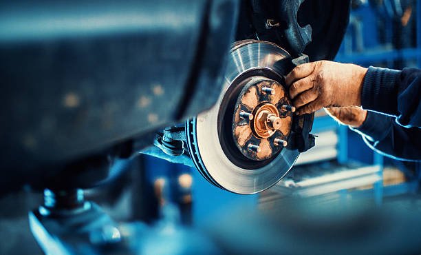 Closeup of unrecognizable mechanic replacing car brake pads. The car is lifted with hydraulic jack at eye level.